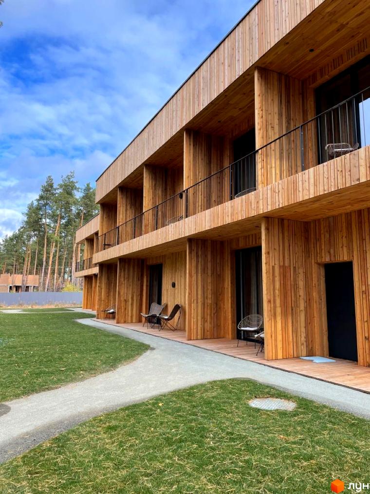 Котеджне містечко КМ Елізіум resort з дерев'яним фасадом та балконами, поруч зелена галявина та доріжка.