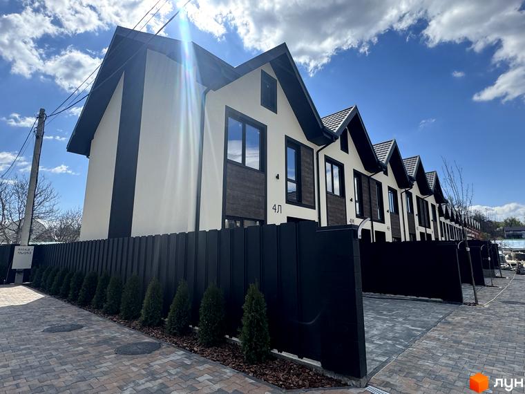 Зовнішній вигляд таунхаусів 40 Estates з чорним парканом та зеленими насадженнями. Територія комплексу викладена бруківкою.