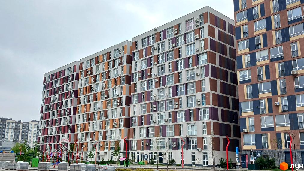 Житловий комплекс Краєвидний - багатоповерхові будинки з різнокольоровими фасадами та кондиціонерами. Поруч дитячий майданчик та будівельні матеріали.