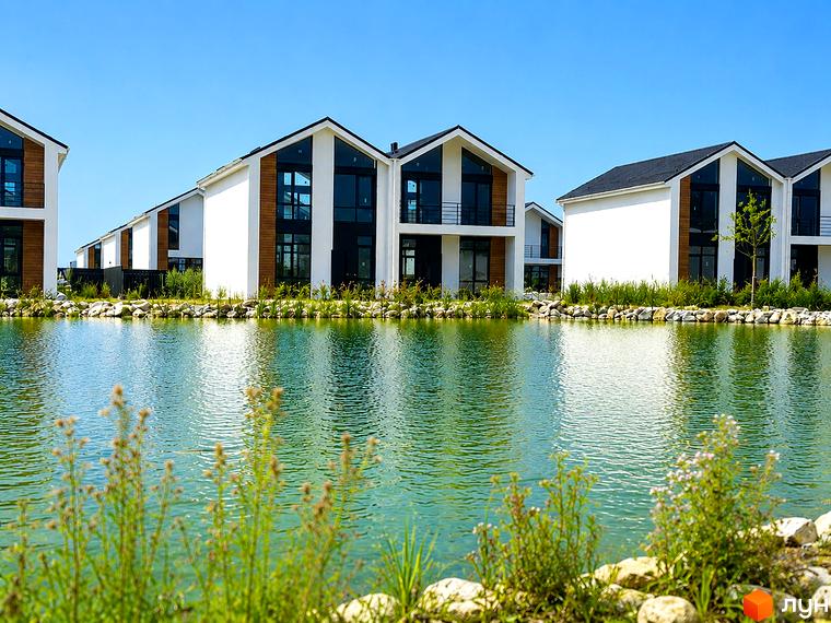 Котеджне містечко КМ Gardd House Eco Village з білими фасадами та дерев'яними елементами, розташоване біля озера з зеленою рослинністю.