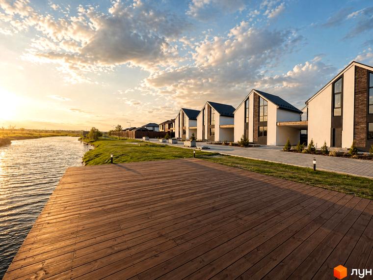 Котеджне містечко КМ DESNA HOMES з сучасними будинками біля річки та дерев'яним настилом. Зелена територія з доглянутими газонами та освітленням.