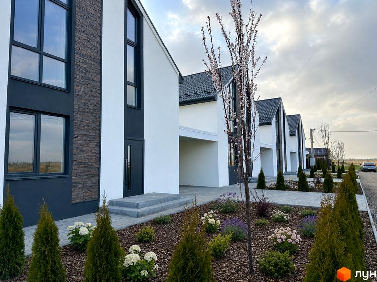 КМ DESNA HOMES: фасади будинків з темними вікнами та кам'яним оздобленням, доглянута прибудинкова територія з деревами та квітами.