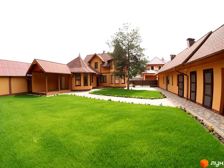 Житловий комплекс КК Містечко Здоров'я з жовтими фасадами, коричневими дахами та доглянутим зеленим газоном. На території комплексу є доріжки з бруківки та квіти.