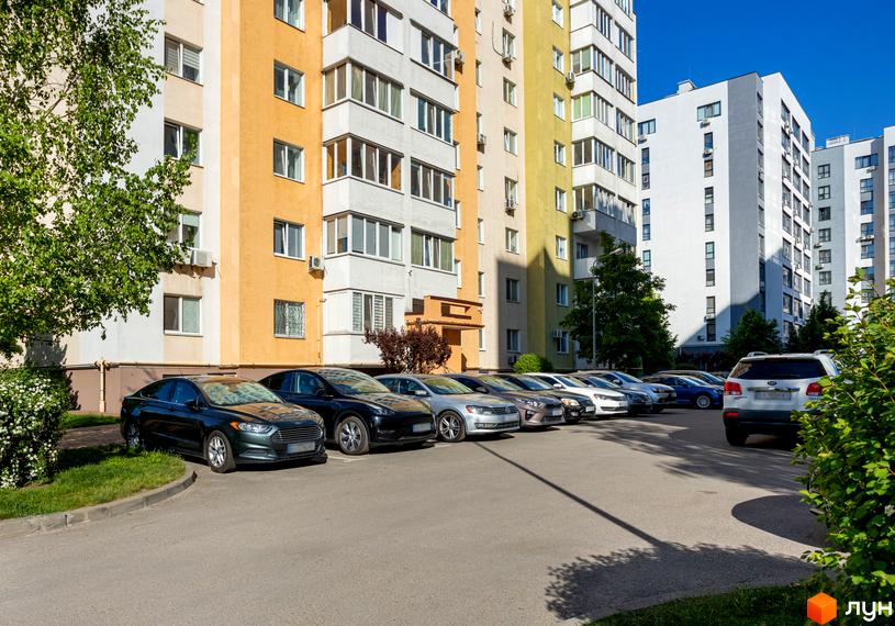 Житловий комплекс Pionerskiy з яскравими фасадами та парковкою автомобілів. Навколо новобудови зелена зона та дерева.