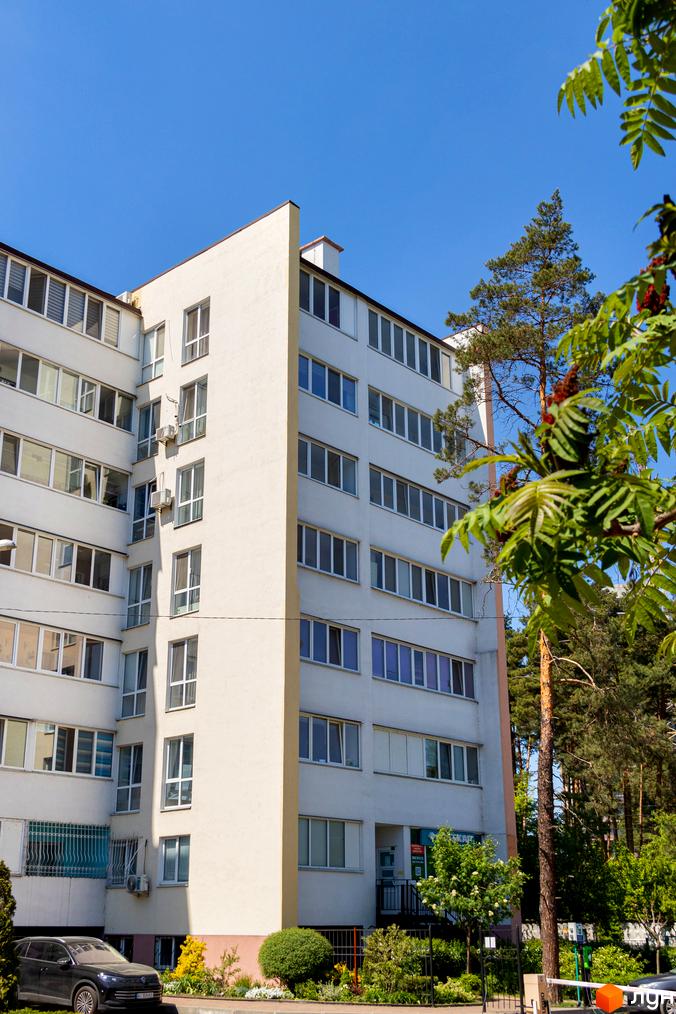 Зовнішній вигляд багатоповерхового будинку житлового комплексу Українка з численними вікнами та балконами, поруч зелена зона та дерева.