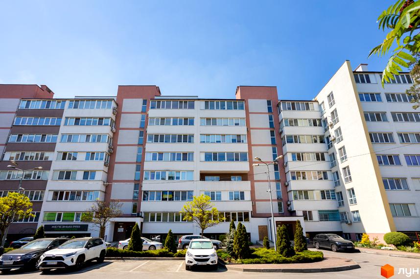 Зовнішній вигляд житлового комплексу "Українка" з багатьма вікнами та балконами, парковка та зелені насадження біля будинку.
