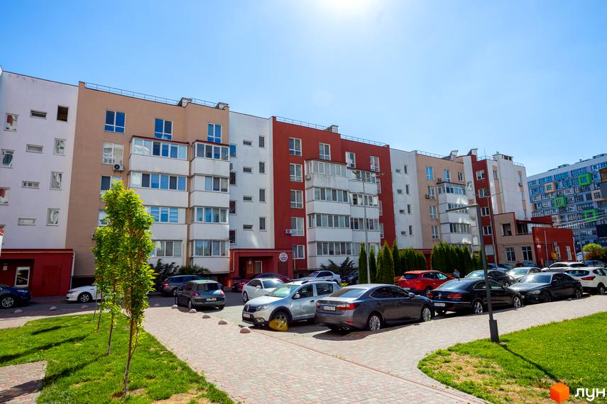 Житловий комплекс Сакура: багатоповерховий будинок з білими, бежевими та червоними фасадами, прибудинкова територія з парковкою, газоном і деревами.