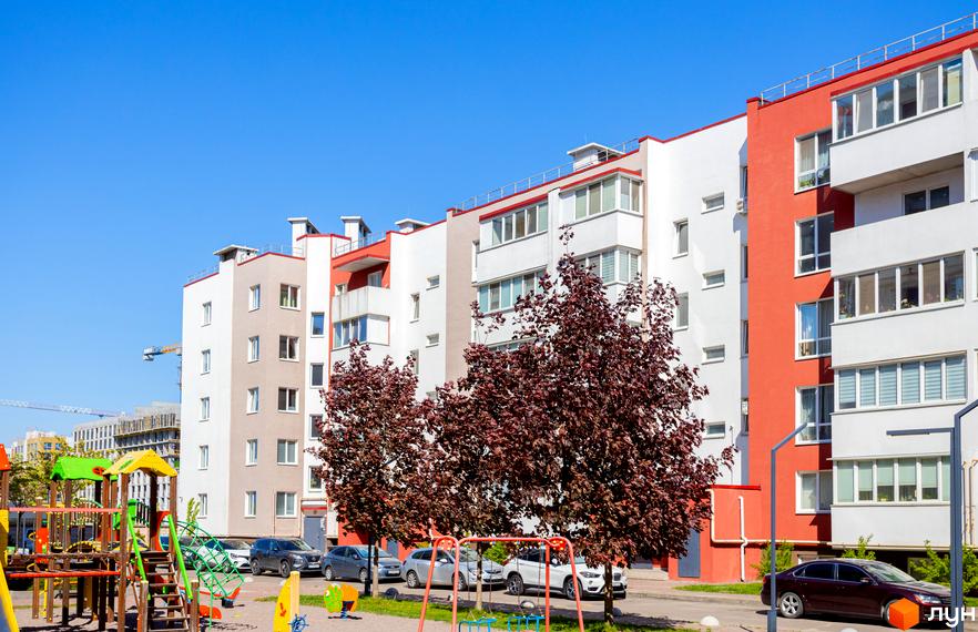 Багатоповерховий будинок Житлового комплексу Сакура з білими та червоними фасадами. Перед ним дитячий майданчик, дерева та припарковані авто.