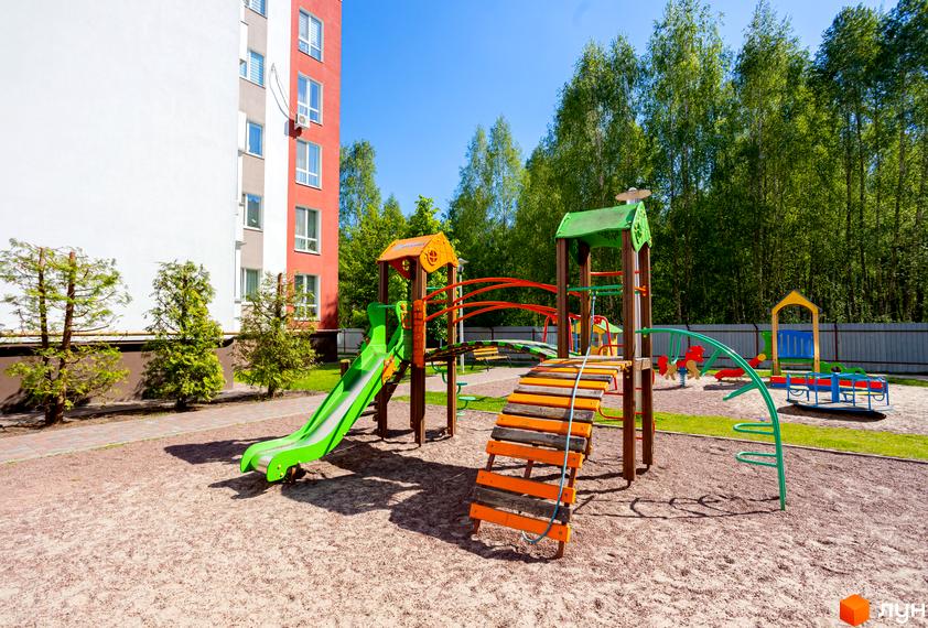 Багатоповерховий будинок Житлового комплексу Сакура з білим та червоним фасадом. На передньому плані дитячий майданчик з гіркою та ігровими елементами.