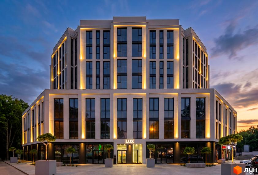 Новобудова Standard LUX з підсвіченим фасадом та великими вікнами. Перед будинком розташовані дерева та доглянута прибудинкова територія.