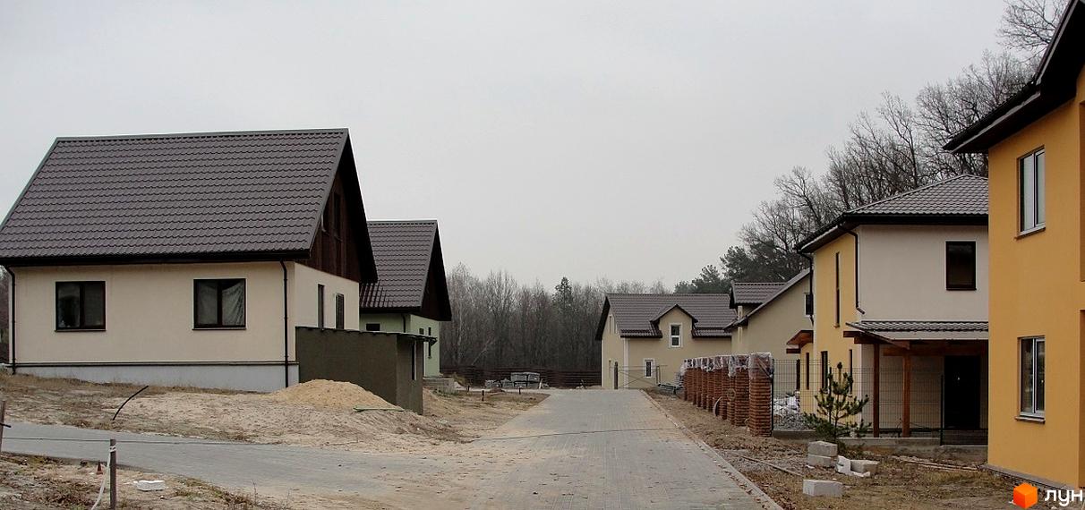 КМ Круглий Озерний: котеджне містечко з однотипними будинками та брукованою дорогою. Навколо новобудов – дерева та ділянки з піском.