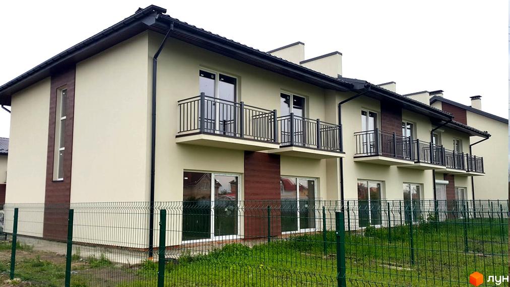 Таунхауси „Новий Київ“: двоповерхові будинки з балконами та великими вікнами, огороджені парканом. Навколо зелена трава та дерева.