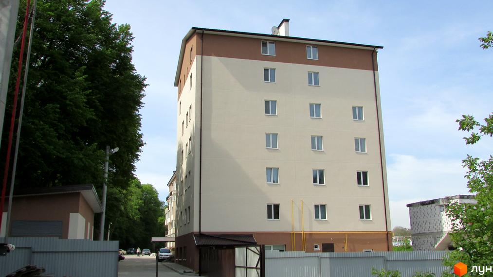 Новобудова на вулиці Піщана, 1. Багатоповерховий будинок світло-бежевого кольору з коричневою верхньою частиною, вікна з білими рамами. Навколо будинку зелені дерева та прибудинкова територія з парканом.