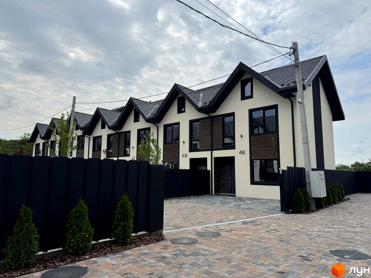 Зовнішній вигляд таунхаусів 40 Estates з темним дахом та світлими стінами, огороджена територія з бруківкою та туями.