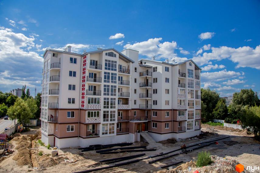 Будівельний проєкт Вишиванка: біла багатоповерхівка з балконами та великими вікнами. Навколо будівельний майданчик з трубами та землею.