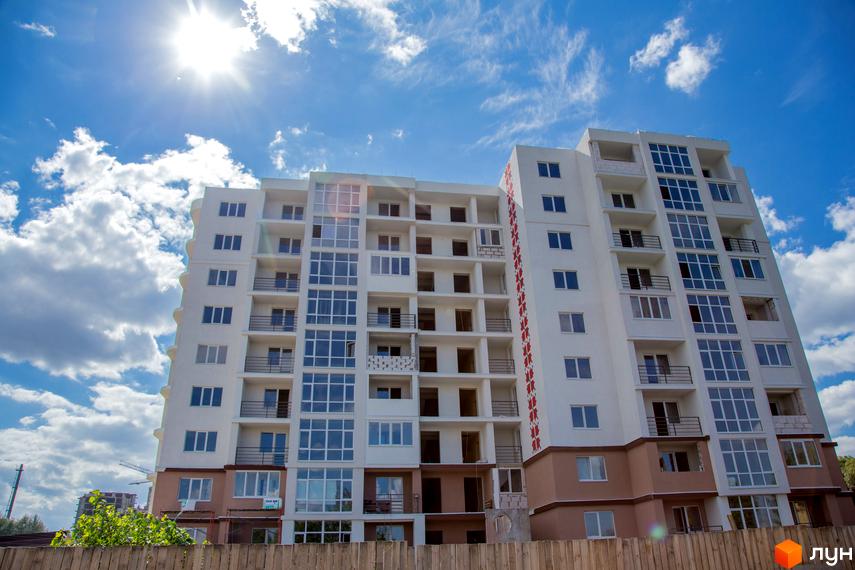 Новобудова ЖК Вишиванка з великою кількістю вікон та балконів на фоні блакитного неба з хмарами. Будинок має білий фасад з коричневим цоколем.