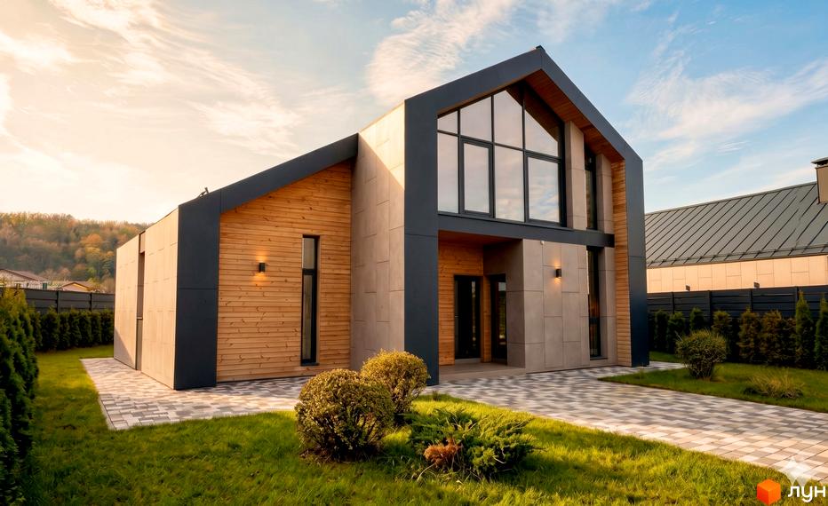 Котеджне містечко КМ Piemont eco village: двоповерховий будинок з дерев'яними та сірими фасадами, великими вікнами, на тлі зеленого газону та бруківки.