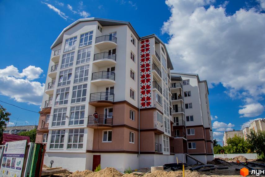 Житловий комплекс Вишиванка. Зовнішній вигляд новобудови з балконами та великими вікнами на тлі блакитного неба з хмарами. Будівельний проєкт з елементами українського орнаменту.