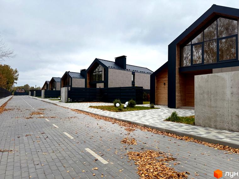 Котеджне містечко КМ Piemont eco village. Сучасні будинки з великими вікнами та дерев'яними елементами, вимощена дорога з опалим листям.