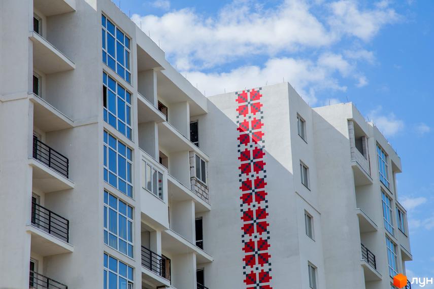 Новобудова ЖК Вишиванка з фасадом, прикрашеним етнічним орнаментом. Сучасний житловий комплекс з балконами та панорамними вікнами на тлі блакитного неба.