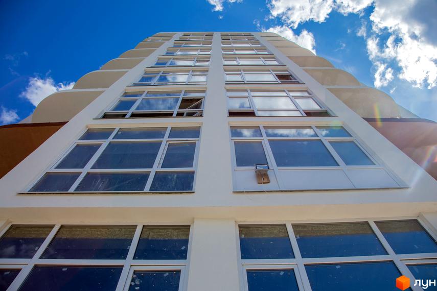 Житловий комплекс Вишиванка – це висотна будівля з великою кількістю вікон. Вона розташована на фоні блакитного неба з хмарами.