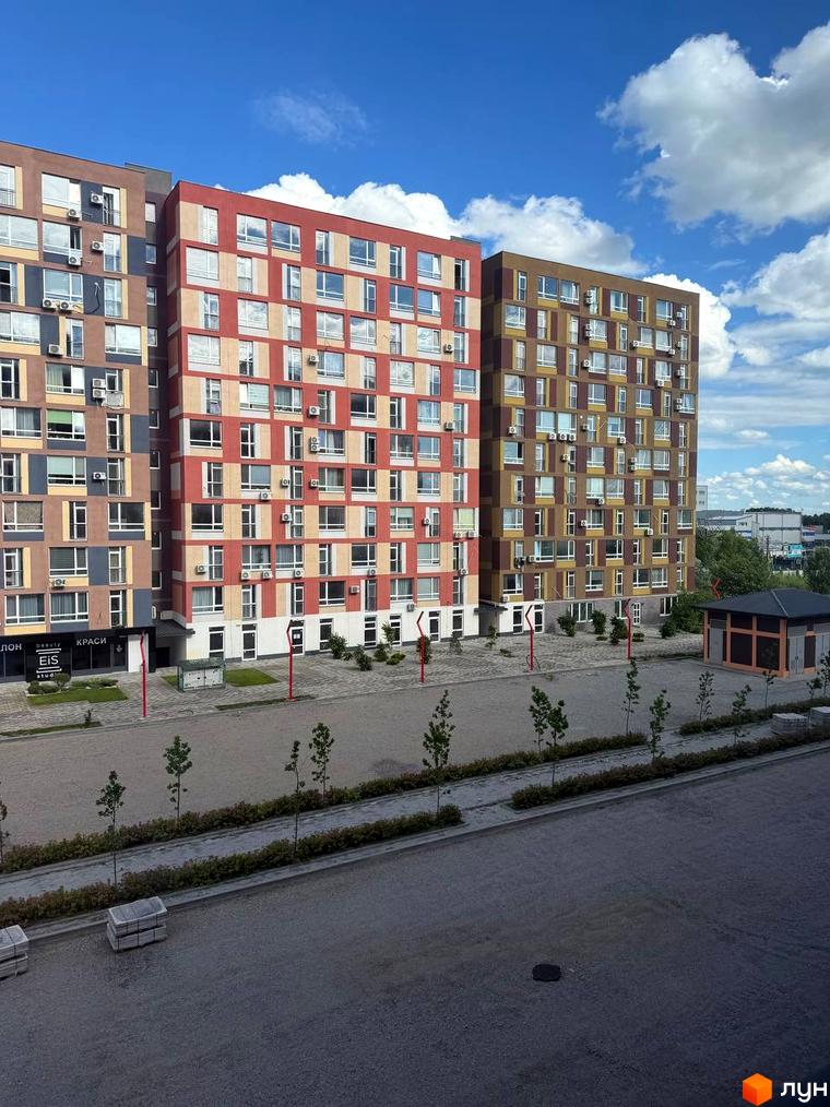 Житловий комплекс Краєвидний: три багатоповерхові будинки з різнокольоровими фасадами. Прибудинкова територія має бруківку та молоді дерева.