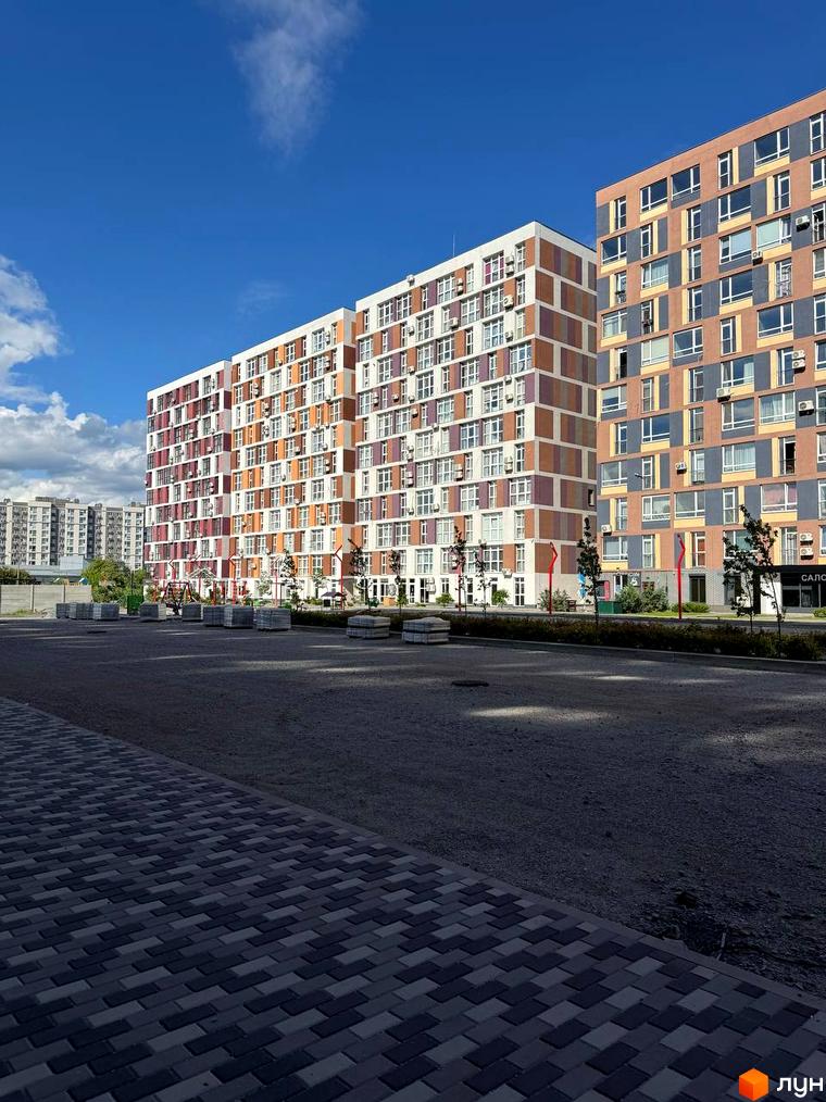 Житловий комплекс Краєвидний: багатоповерхові будинки з різнокольоровими фасадами, облаштована прибудинкова територія з дитячим майданчиком та бруківкою.