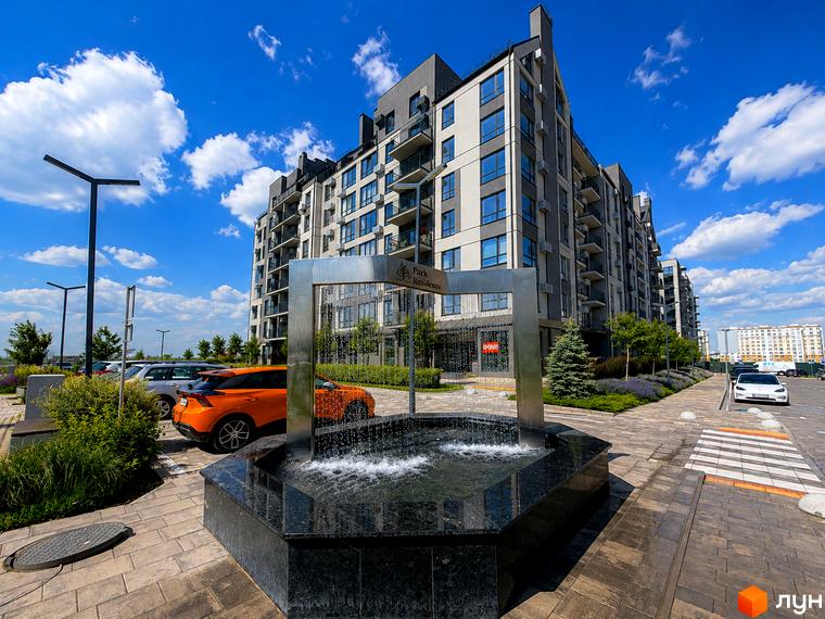 Новобудова Park Residence з фасадами сірого та білого кольорів, з численними балконами та панорамними вікнами. Поруч розташована прибудинкова територія з фонтаном, зеленими насадженнями та парковкою.