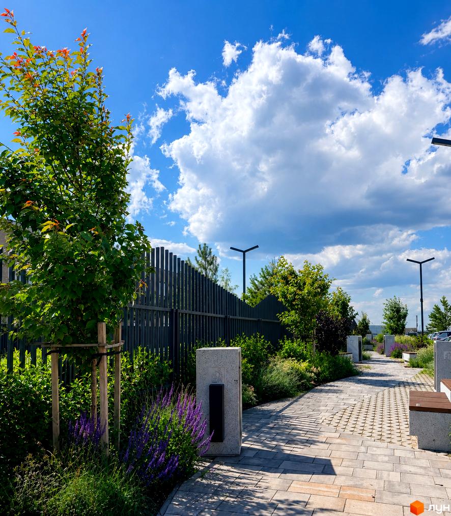 Прибудинкова територія Житлового комплексу Park Residence з доріжкою, зеленими насадженнями, фіолетовими квітами та вуличними ліхтарями.