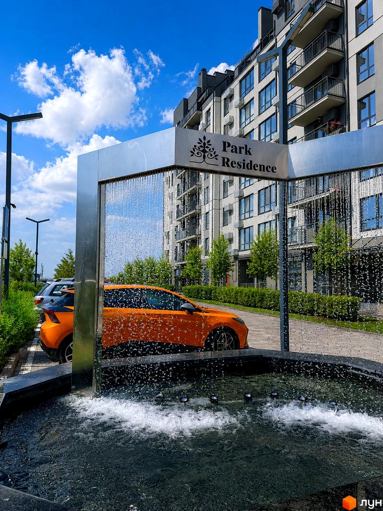 Новобудова Park Residence з фасадом з панорамних вікон та балконів. Поруч розташована прибудинкова територія з фонтаном та автомобілями.