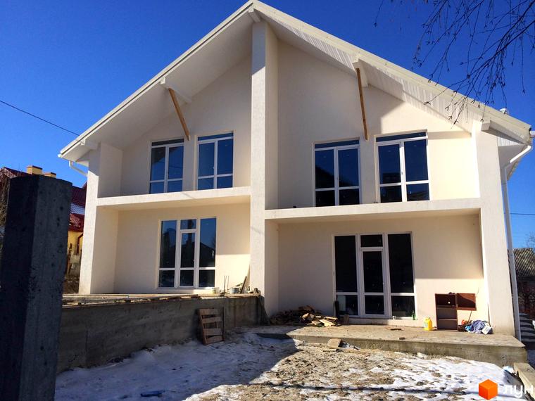 Котеджне містечко КМ Поршна-Наварія: двоповерховий будинок з великими вікнами та балконом на другому поверсі. Територія навколо будинку частково вкрита снігом, видно будівельні матеріали.