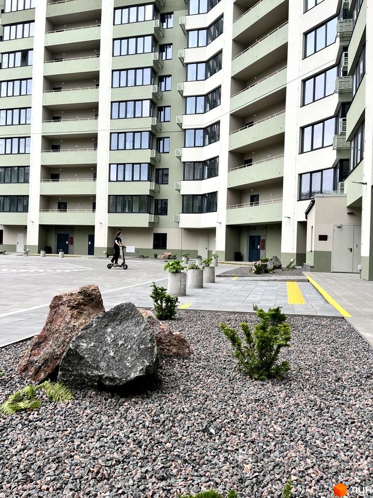Багатоповерховий будинок Житлового комплексу GRANIT з світло-зеленими фасадами. Прибудинкова територія облаштована мощенням, камінням та рослинами.