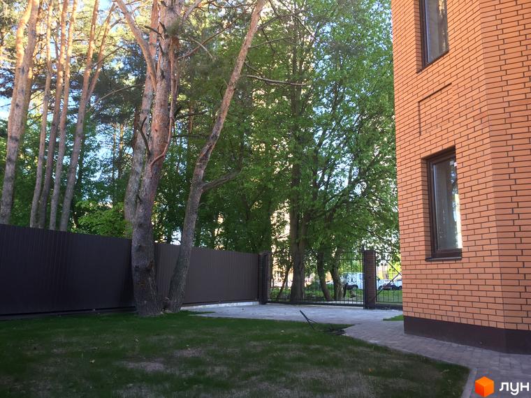 Зовнішній вигляд цегляної новобудови ЖК Соборна Фортеця з вікнами та парканом. Прибудинкова територія з газоном та деревами.