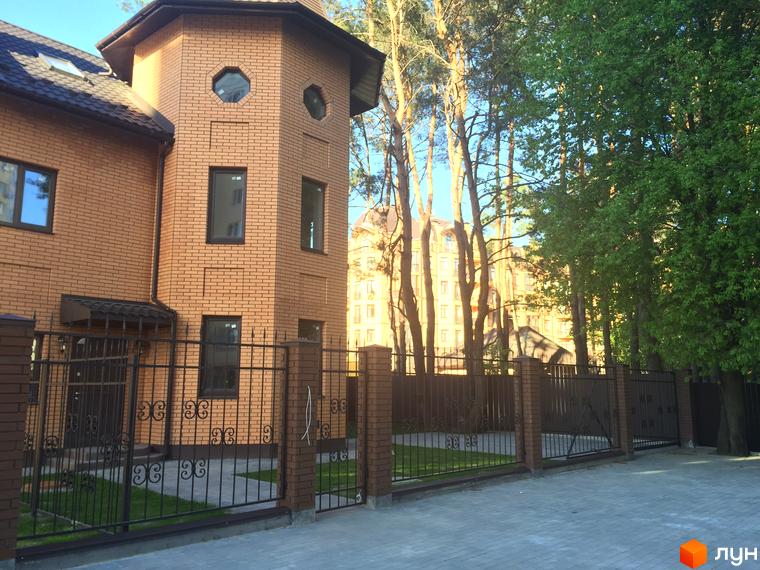 Житловий комплекс Соборна Фортеця: цегляний будинок з вікнами незвичайної форми, огороджений кованим парканом. Прибудинкова територія з доглянутим газоном та бруківкою.