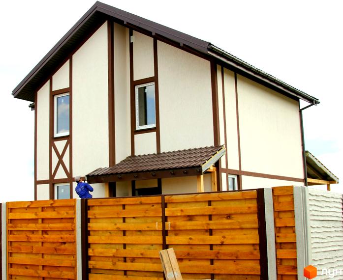 Котеджне містечко Альпійський Хуторок: двоповерховий будинок з коричневими віконними рамами та дахом, огороджений дерев'яним парканом.