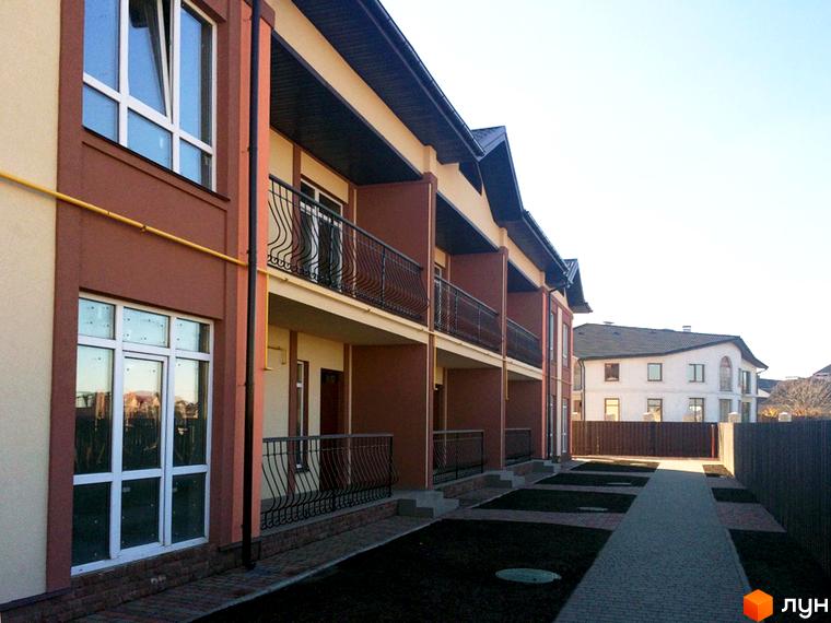 Таунхаус СанЛенд. Зовнішній вигляд двоповерхових будинків з балконами та вікнами. Прибудинкова територія з доріжкою та газоном.