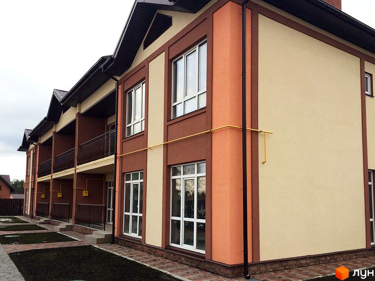 Таунхаус СанЛенд з коричневими та бежевими фасадами, балконами та вікнами. Прибудинкова територія з газоном та доріжками.