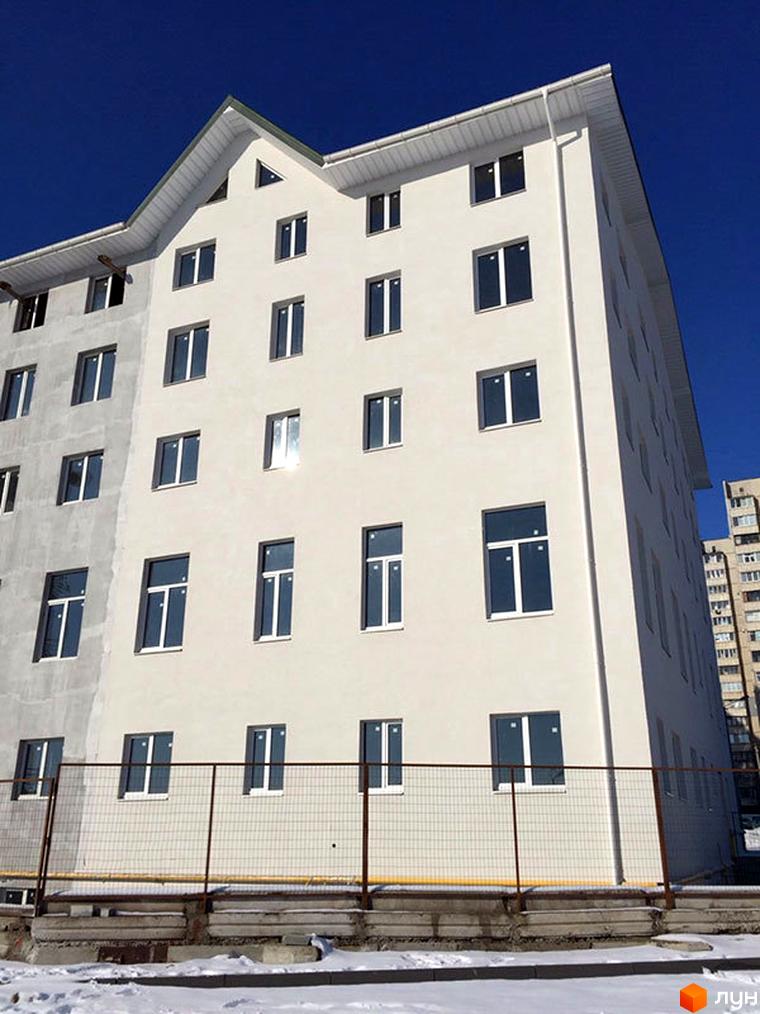 Зовнішній вигляд новобудови ЖК Титаренківський з численними вікнами та білим фасадом. На передньому плані видно паркан та засніжену територію.