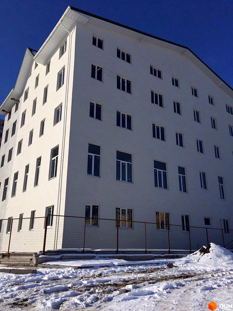 Житловий комплекс Титаренківський. Біла багатоповерхова новобудова з численними вікнами під синім небом. Навколо будівлі огороджена територія з парканом та засніжена ділянка.