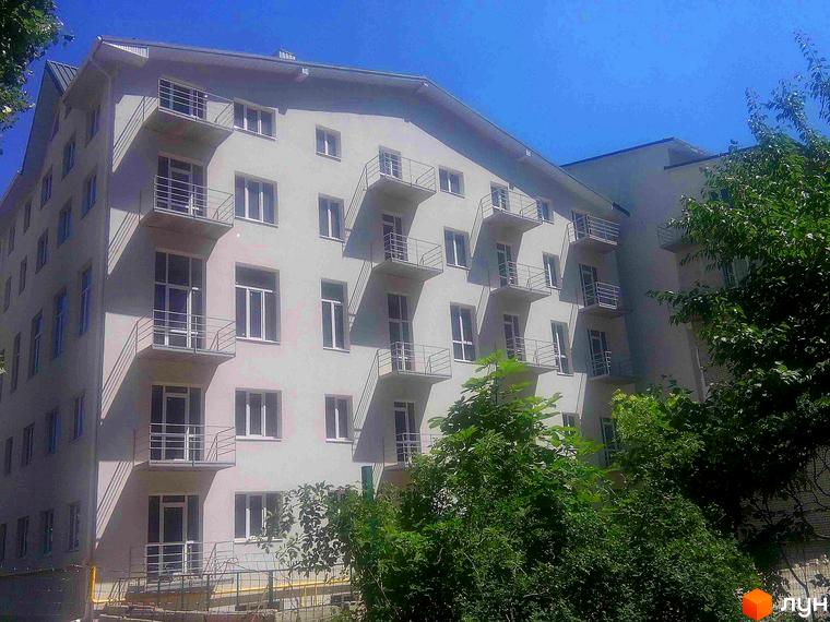 Фасад житлового комплексу Титаренківський з балконами та вікнами на тлі блакитного неба. Навколо будівлі зелені дерева.