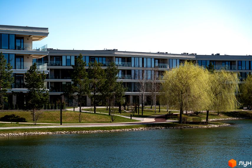 Житловий комплекс Park Lake City з багатоповерховими будинками, великими вікнами та балконами. На передньому плані озеро, зелені газони, дерева та доріжки.