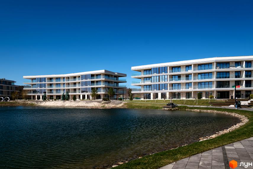 Житловий комплекс Park Lake City: білі будинки з великими вікнами та скляними балконами, розташовані біля озера з зеленою територією.