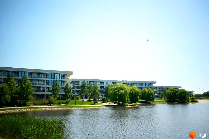 Житловий комплекс Park Lake City з багатоповерховими будинками та балконами, розташований біля озера з зеленою зоною та деревами.