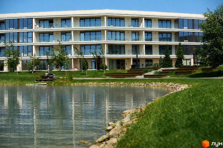 Новобудова Park Lake City з панорамними вікнами та балконами, розташована біля озера з доглянутою зеленою територією.