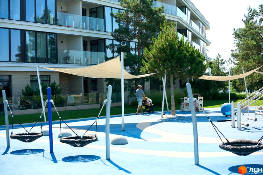 Житловий комплекс Park Lake City: багатоповерховий будинок з великими вікнами та балконами, поруч дитячий майданчик з гойдалками та пісочницею.