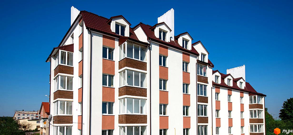 Фасад житлового комплексу на вул. Коцюбинського, 1. Будинок має біло-коричневий фасад, червоний дах та багато вікон і балконів. Навколо зелені дерева та сусідні будівлі.