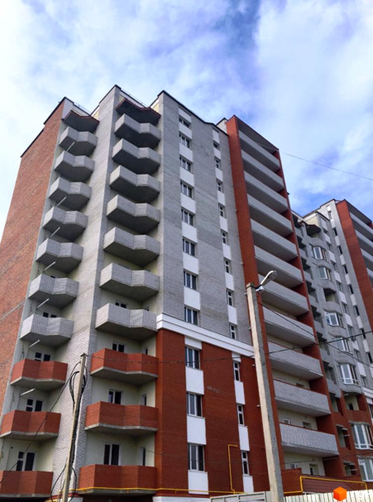 Житловий комплекс Левада: багатоповерхова будівля з цегляними та сірими фасадами, численними балконами на тлі хмарного неба.