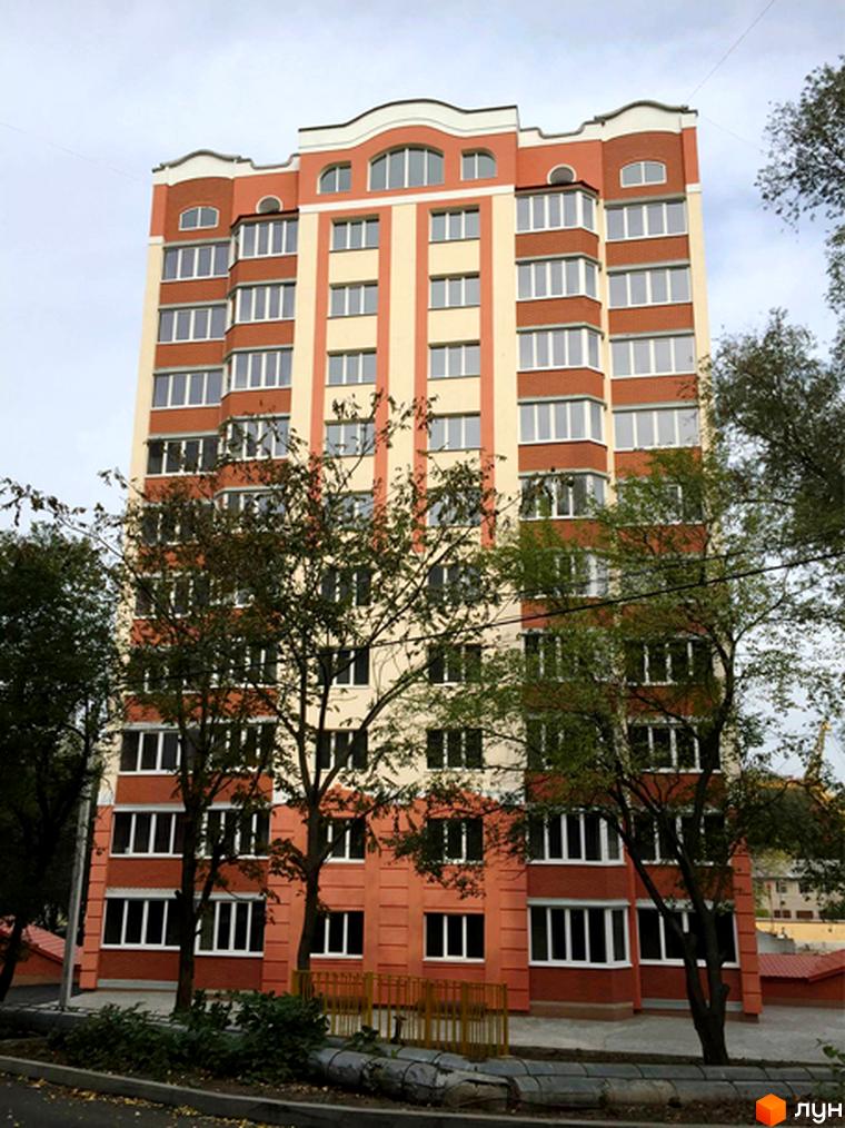 Зображення фасаду багатоповерхового будинку в Житловому комплексі Родинний затишок. На передньому плані видно дерева та частину прибудинкової території.