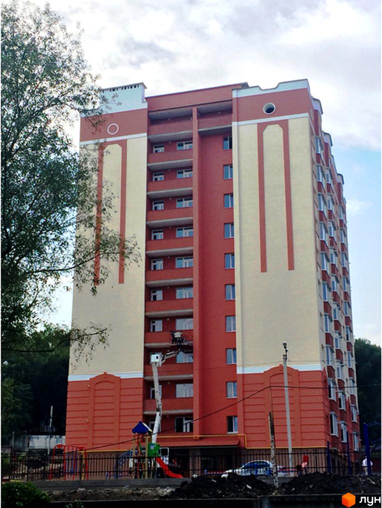 Зображення багатоповерхового будинку Житловий комплекс Родинний затишок з червоно-бежевим фасадом. На передньому плані дитячий майданчик та зелені насадження.