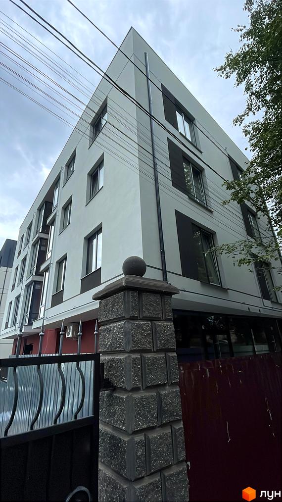 Фасад житлового комплексу на вул. Петра Дорошенка, 66а зі світлими стінами, темними вікнами та балконами. Поруч видно кам'яний стовп огорожі та дерева.